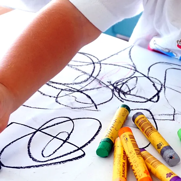 クレヨンで線を描く小さな子の手元