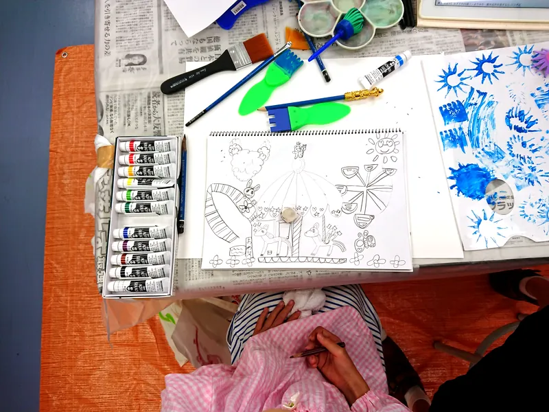 机に並んだ絵の具のチューブと描きかけの絵