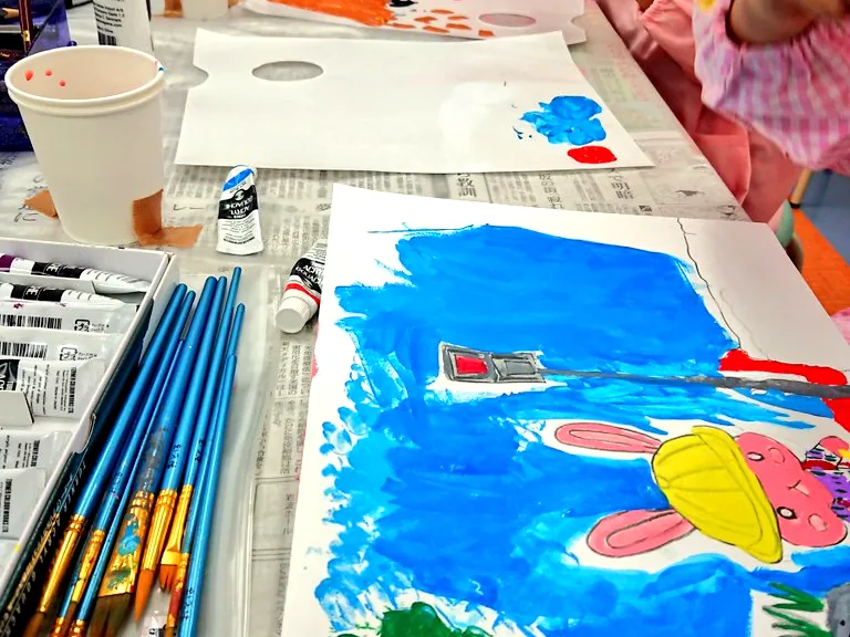 絵の具と筆で描く子供の手元と描きかけの絵